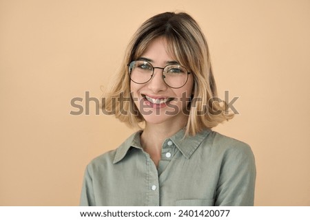 Smiling pretty gen z blonde young woman, happy college student girl with short blond hair wearing glasses looking at camera standing isolated on beige background. Close up headshot portrait.