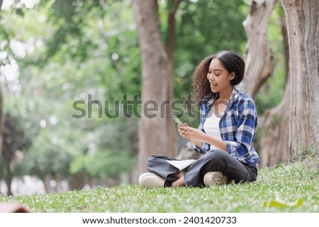 Young African American woman using smartphone sitting and relaxing at green park outdoor.