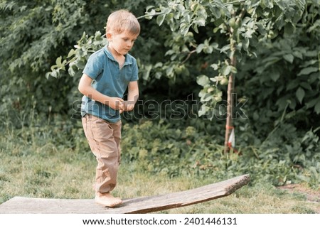 First steps to balance, nature's playground. Young boy on makeshift balance beam crafted from fallen tree limb, exploration of coordination, moment of concentration and growth. Royalty-Free Stock Photo #2401446131