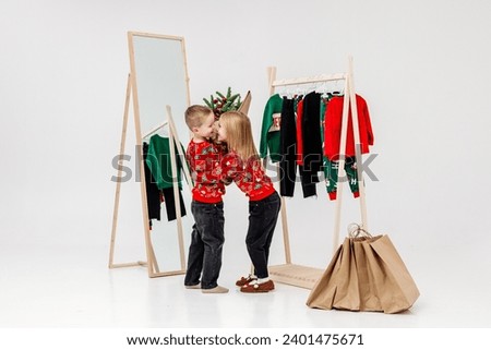 Children on a light background in a dressing room against the background of hangers with children's clothes. Little fashionistas on the eve of Christmas night.