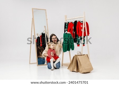 Beautiful happy young mother with her daughter on the background of hangers with fashionable clothes. Family enjoying shopping. Promotional clothing concept.