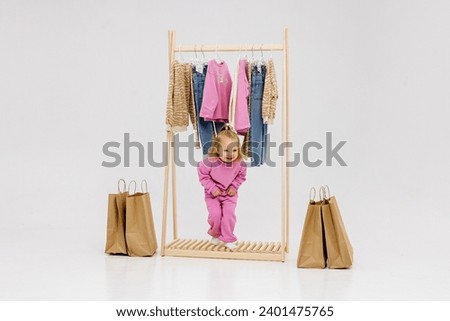 A child, a little girl, stands near the closet, chooses clothes against a light background. Dressing room with clothes on hangers. Wardrobe of children's and stylish clothes. Montessori wardrobe.