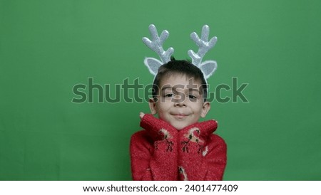 Cute boy with christmas headbank reindeer antlers posing isolated on green background. High quality photo