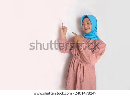 Happy Asian muslim woman showing finger after voting on Indonesia presidential election Royalty-Free Stock Photo #2401478249