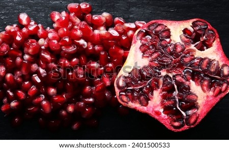 Macro photography of an organic pomegranate cut in half and of a handful of pomegranate seeds on slate background for food illustrations