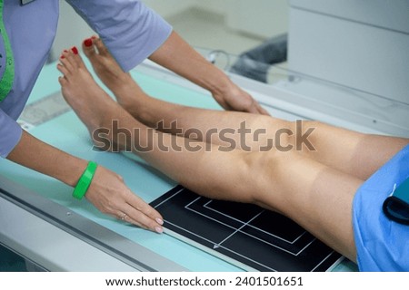 Experienced radiographer preparing adult person for knee radiography Royalty-Free Stock Photo #2401501651