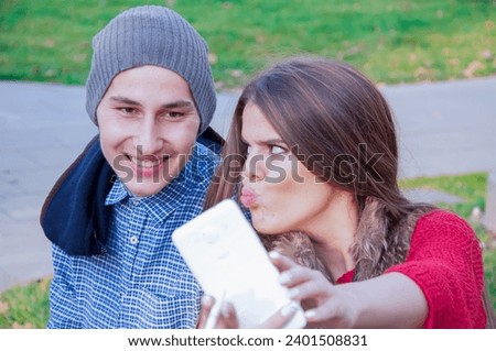 We are in love. Attractive young couple is taking autumn selfie in the public park covered with fallen leaves