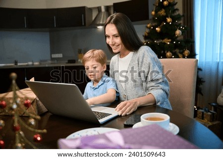 Woman with little boy watching cartoons on laptop at home during winter holidays
