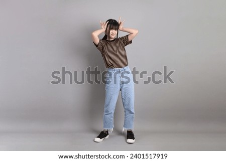 The full length of young adult Asian woman standing on the grey background.
