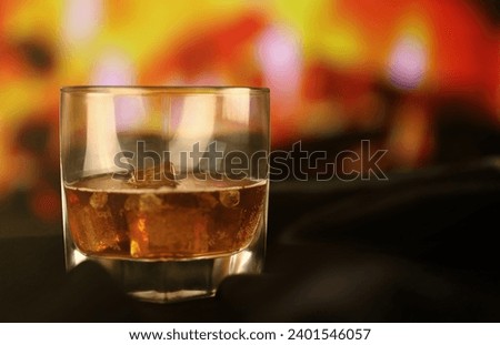 Whisky or whiskey or bourbon with ice on wooden surface on fireplace background. Luxury elite alcohol in wide glass. Low key dark scene