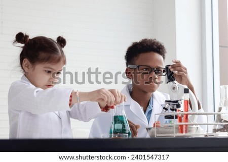 Happy African boy in lab coat doing science experiment with little cute girl buddy friend, young school kid scientist having fun in chemistry laboratory, little children doing research at school. Royalty-Free Stock Photo #2401547317