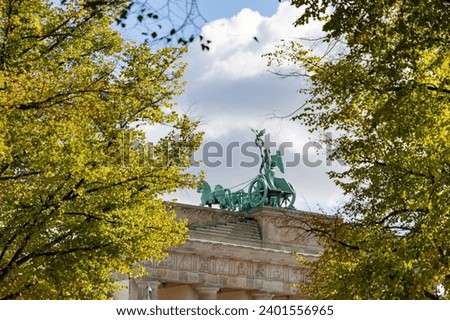 A picture of the quadriga statue atop the Brandenburg Gate as seen between nearby autumn foliage.