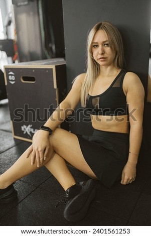 Young woman with serious face sits on floor in sports bra. Moment of rest and reflection during workout session in sports club Royalty-Free Stock Photo #2401561253