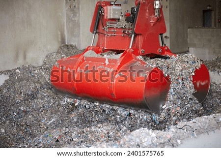 A red bridge crane grab during Waste derived fuel handling. Processing of municipal solid waste into an energy source. Royalty-Free Stock Photo #2401575765