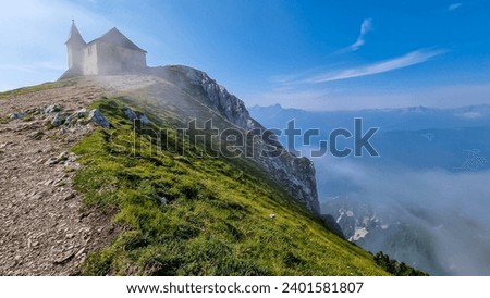 Scenic hiking trail at sunrise to chapel Maria am Stein on top of mountain peak Dobratsch, Villacher Alps, Austria, Europe. Looking alpine meadow at morning. Golden morning hour tranquil atmosphere Royalty-Free Stock Photo #2401581807