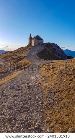 Scenic hiking trail at sunrise to chapel Maria am Stein on top of mountain peak Dobratsch, Villacher Alps, Austria, Europe. Looking alpine meadow at morning. Golden morning hour tranquil atmosphere Royalty-Free Stock Photo #2401581913