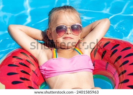 Cute little girl lying on inflatable circle in swimming pool with blue water on warm summer day on tropical vacations. Cute little girl sunbathing on air mattress