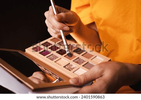 Unrecognizable woman holds a palette with a make-up brush in her hands, a close up photo. Concept of home makeup.
