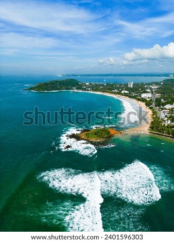 Aerial view of turquoise waters, tropical peninsula, white waves kiss sandy beaches with lush greenery in the backdrop, an idyllic scene for travel agencies, postcards, or romantic getaways.