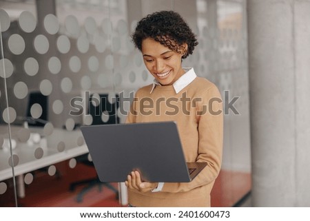 Pretty female freelancer working on laptop while standing on modern coworking background