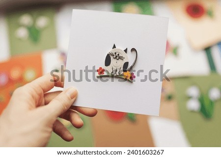 Hand holding quilling card with cute cat. woman making greeting cards. Hand made of paper quilling technique. Handicraft at home. Hobby, home office.