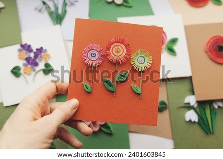 Hand holding quilling card with flowers. woman making greeting cards. Hand made of paper quilling technique. Handicraft at home. Hobby, home office.