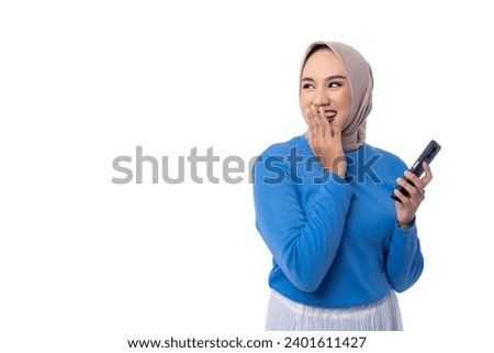 Beautiful happy young Asian woman holding mobile phone, looking at empty copy space area with surprised expression isolated on white background