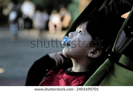Exterior close up portrait photo view by night of a young baby kid child children infant kid male eurasian asian boy with a dummy teat looking up at something in a park garden in the evening alone