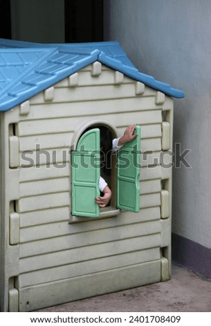 Hong Kong, Asia - 03 13 2010 : Exterior photo view of young baby kid child children infant kid opening or closing the window shutters of plastic house house in a court yard of playground kindergarten