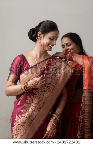 Two Indian women dressed in traditional sarees are adjusting their attire. Royalty-Free Stock Photo #2401722481