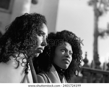 Side portrait of two female friends looking away outdoors. It is a monochrome analog film image made with a medium format old camera. It is a sunny cold winter day.