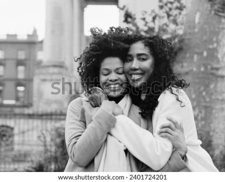 Two female black friends hugging each other in the street. It is a monochromatic image make withe medium format analog camera. it is a cold winter day and they are wearing thick coats.