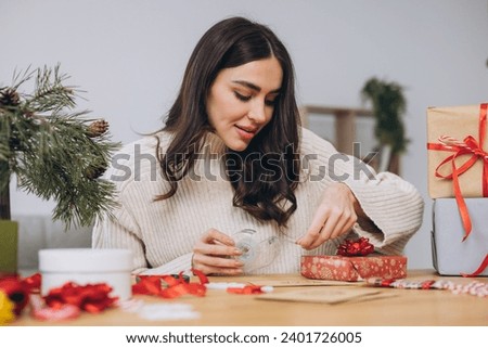 Woman wrapping Christmas gift boxes, close up. Unprepared presents on table with decor elements and items Christmas or New year DIY packing Concept.