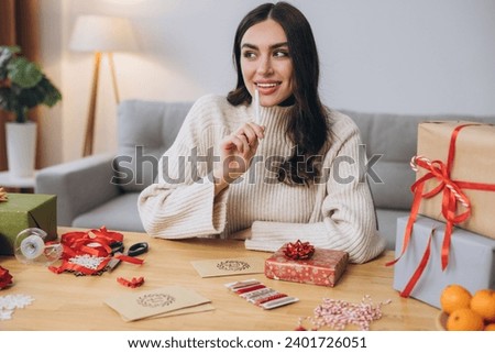 Beautiful happy woman is packing and signing greeting card for New Year and Christmas