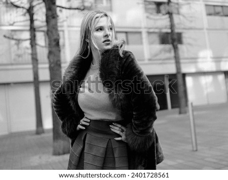 Film portrait of fashion model posing in the street in a cold winter day. She is wearing a fake fur coat, a sweater and skirt. Monochrome portrait.