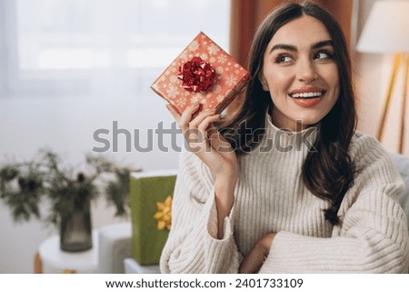 Beautiful happy woman unwrapping New Year or Christmas presents at home on sofa