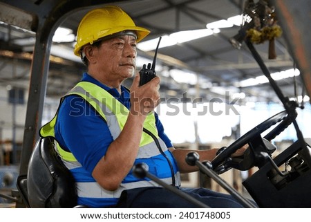 senior worker using walkie talkie and holding steering wheel on forklift truck in the factory