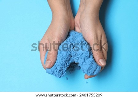 Woman playing with kinetic sand on light blue background, top view Royalty-Free Stock Photo #2401755209