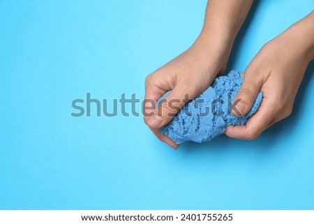 Woman playing with kinetic sand on light blue background, top view. Space for text Royalty-Free Stock Photo #2401755265