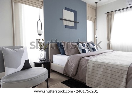 Stylish Bedroom with gray fabric headboard and bed with soft blue and white pillows setting. Cozy bedroom with art wall. Royalty-Free Stock Photo #2401756201