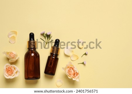 Bottles of cosmetic serum, beautiful flowers and petals on pale yellow background, flat lay. Space for text
