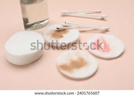 Dirty cotton pads after removing makeup, buds and bottle of cosmetic product on beige background, closeup
