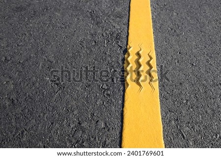 Tire marks on reflective yellow stripes. Close up bumps in traffic lines on black asphalt road background with copy space with selective focus.