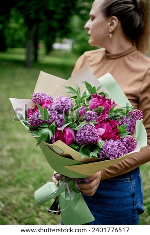 Woman holds bouquet park spring lilac peonies green leaves ribbon brown top blue jeans blurred effect.