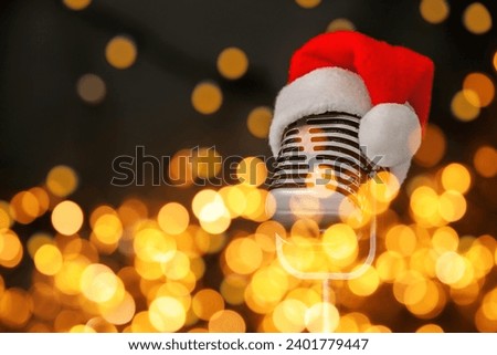 Christmas music. Microphone with Santa hat on black background, bokeh effect