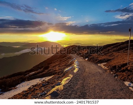 Panoramic hiking trail at sunrise to summit Dobratsch in Carinthia, Austria, Europe. View of silhouette of endless mountain ranges Julian Alps and Karawanks. Alpine valley is covered by mystical fog Royalty-Free Stock Photo #2401781537