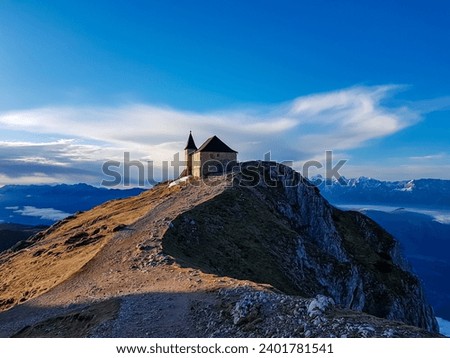 Scenic sunrise view of chapel Maria am Stein on top of mountain peak Dobratsch, Villacher Alps, Austria, Europe. Looking at Julian and Karawanks mountain range. Golden morning hour tranquil atmosphere Royalty-Free Stock Photo #2401781541