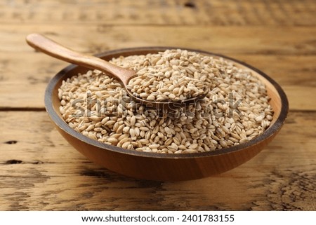 Dry pearl barley in bowl and spoon on wooden table, closeup Royalty-Free Stock Photo #2401783155