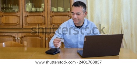 Image of a man in front of a PC holding a credit card while making online purchases
