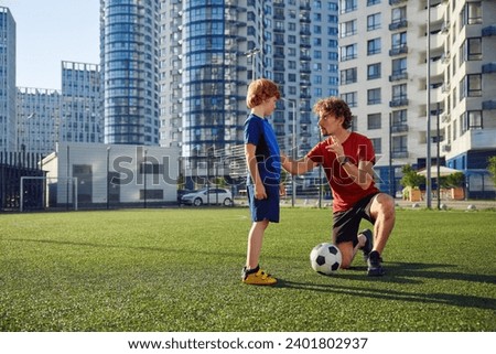 Father teaching son child to play football on city stadium Royalty-Free Stock Photo #2401802937